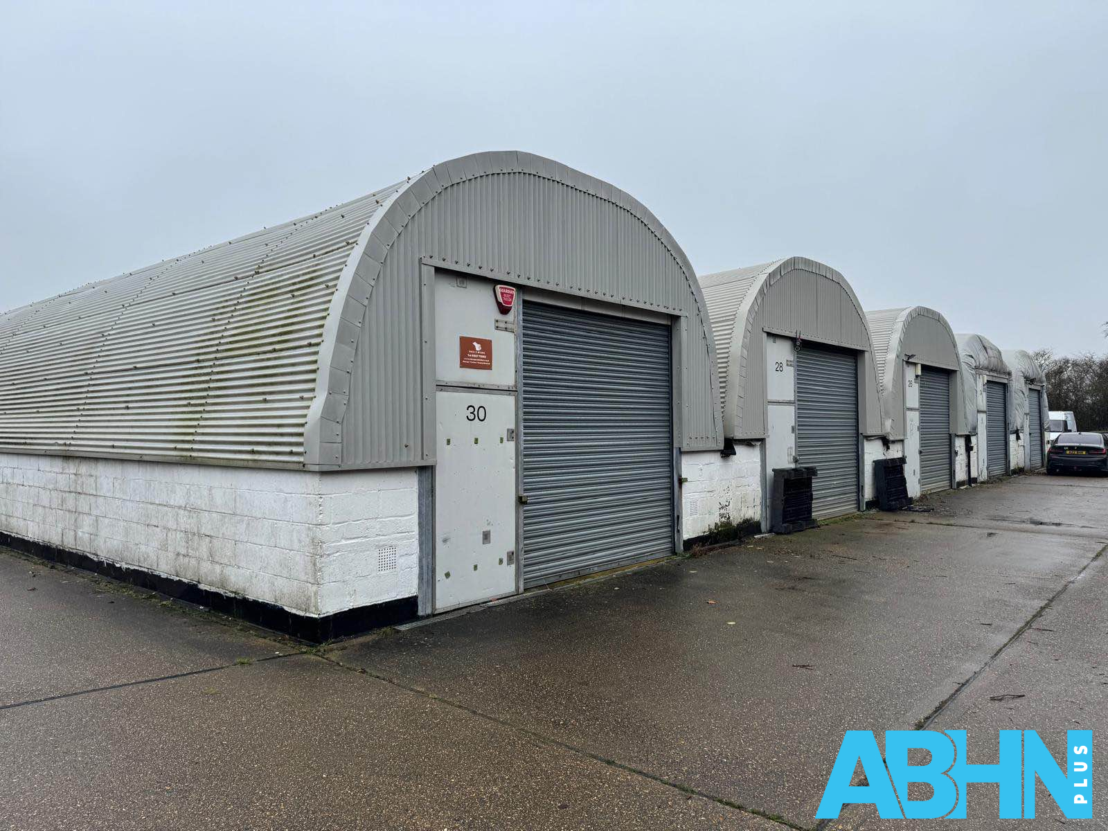 Row of curved-roof storage units with metal garage doors, labeled '30' and others, under an overcast sky.