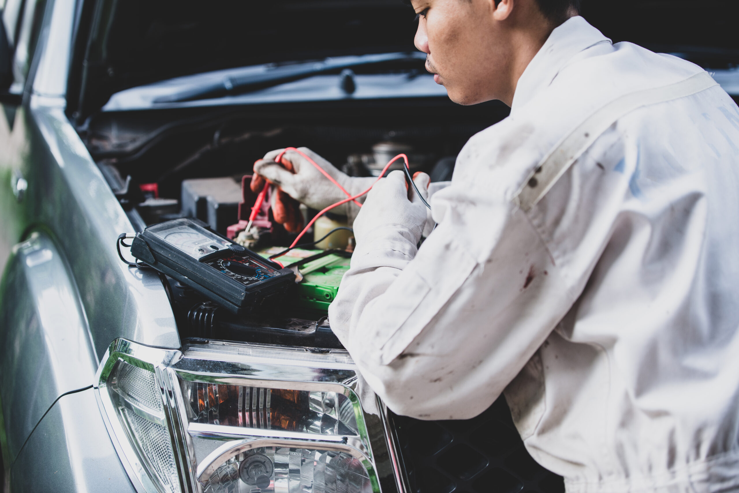 Mechanic testing a car parts battery and alternator using a multimeter to ensure optimal performance and reliable power delivery to the starter and electrical systems.