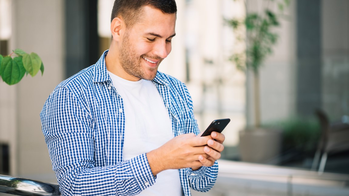 Smiling man in a checkered shirt using his smartphone while experiencing effortless online shopping high-quality auto parts.